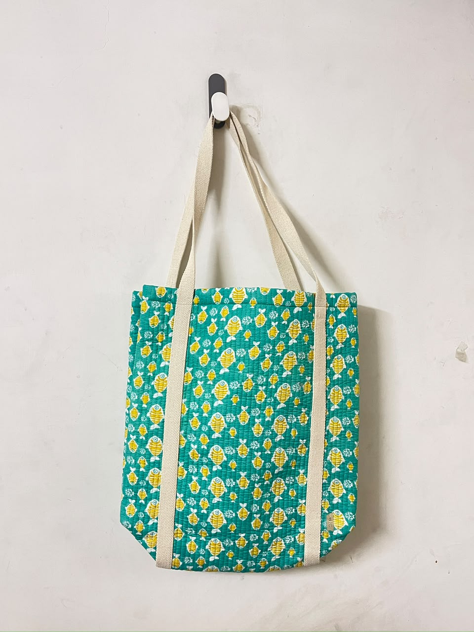 A fabric tote bag with a teal green and yellow floral pattern, featuring beige canvas shoulder straps